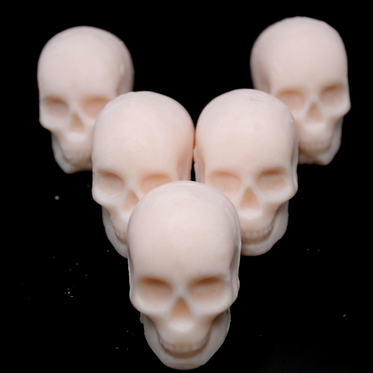 Five skull-shaped wax melts arranged in an arrowhead formation on a black background, each skull partially peeking from the one in front. The front skull stares directly into the camera, creating a bold, eerie aesthetic perfect for gothic decor, spooky ambiance, and macabre wax enthusiasts.
