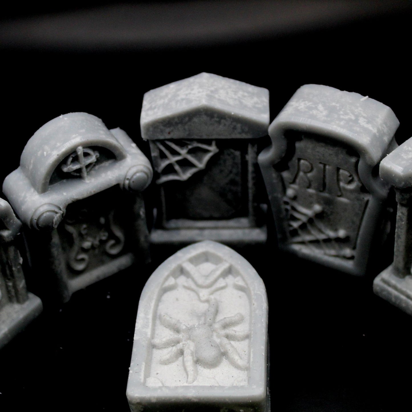 3/4 top-down view of five tombstone-shaped wax melts on a black background, with four standing upright encircling a fifth lying flat in the center. A haunting, gothic aesthetic perfect for spooky home decor, macabre ambiance, and alternative wax melt lovers.