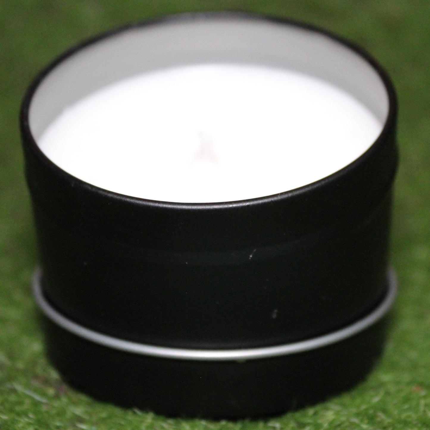 Black metal candle tin holding a white candle, photographed on grass. Handmade Skyrim-inspired candle with soy wax in a reusable container - perfect for unique home decor, gifts, and personal expression.