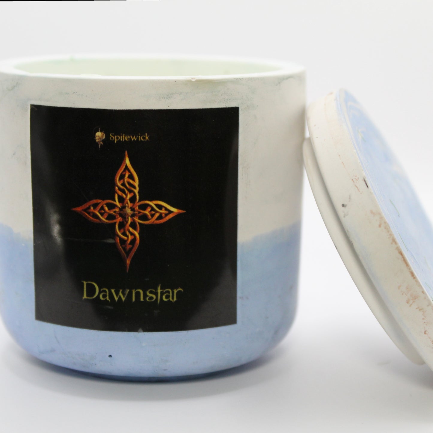 A white and blue candle holder with a black label featuring a four-pointed star in elegant gold Celtic knotwork. The name dawnstar is displayed in gold beneath the intricate design, adding a bold, mystical touch. The lid is removed and propped against the right side, showcasing the full aesthetic. Set against a clean white background, this handcrafted candle merges tradition and modern artistry, perfect for unique home decor, gifts, and personal expression.