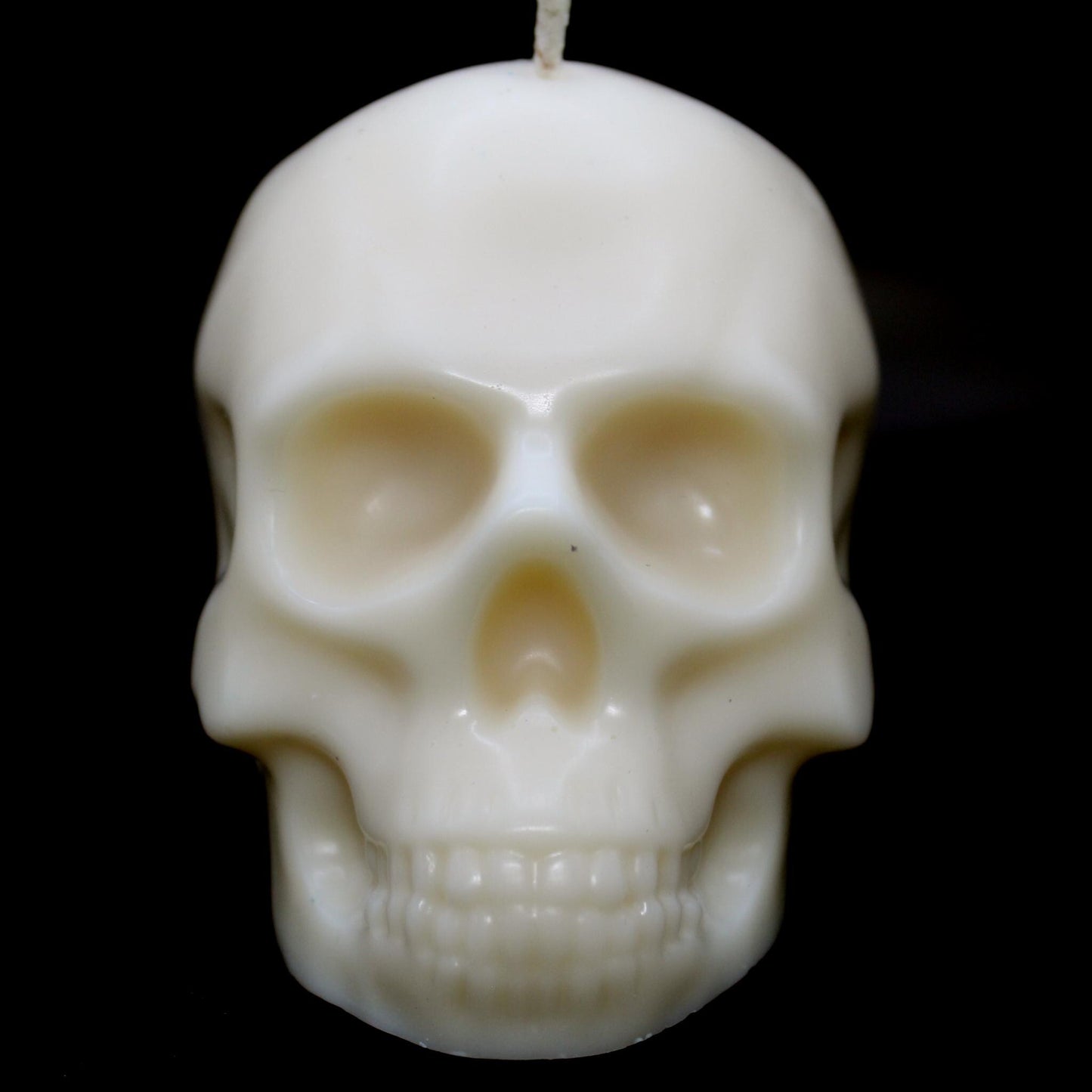 White skull-shaped wax candle set against a black background, staring directly into the camera with an eerie, haunting presence. A bold gothic decor piece perfect for dark aesthetic lovers, spooky home accents, and macabre candle enthusiasts."