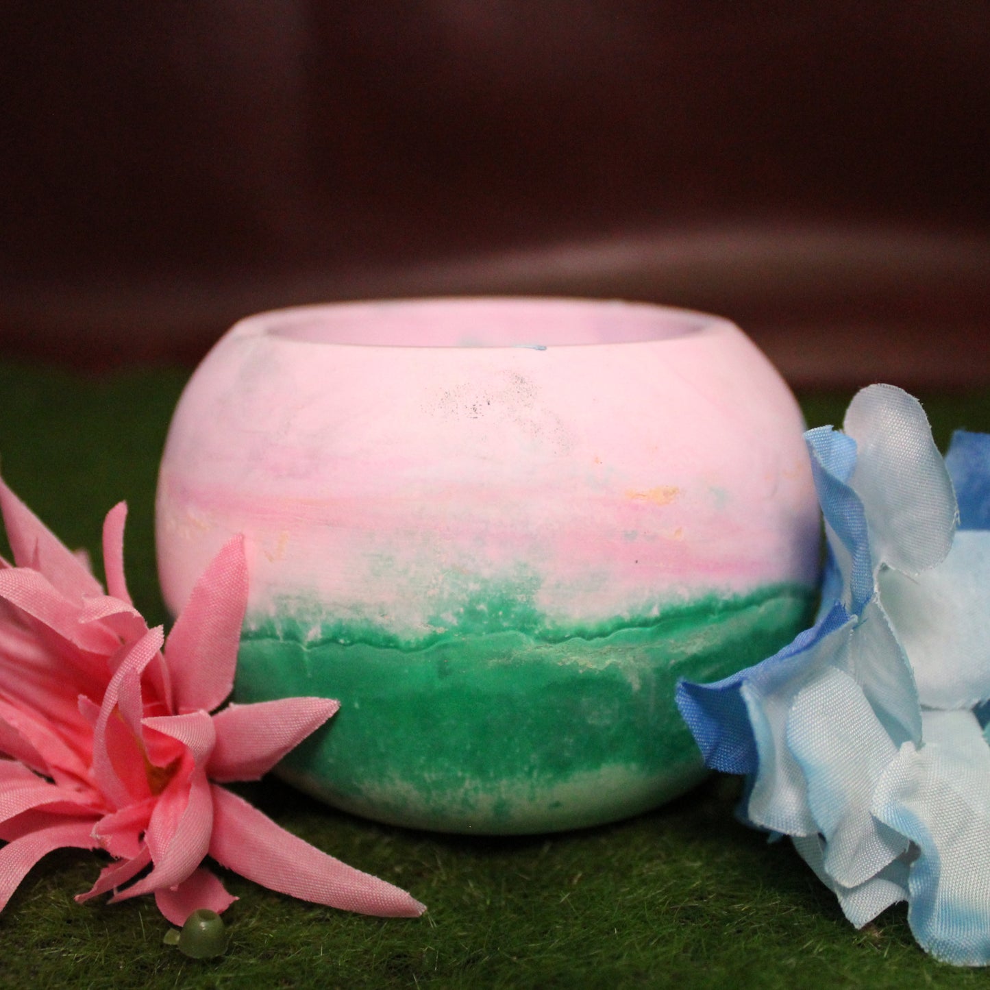 Handcrafted candle holder featuring the pink, blue, and green hues of the polysexual pride flag, seamlessly blended together for a striking design. Set on grass with a burgundy vinyl backdrop, surrounded by an assortment of flowers mirroring the flag’s colors, creating a visually rich and identity-affirming scene. Perfect for LGBTQ+ home decor, pride gifts, and statement lighting.