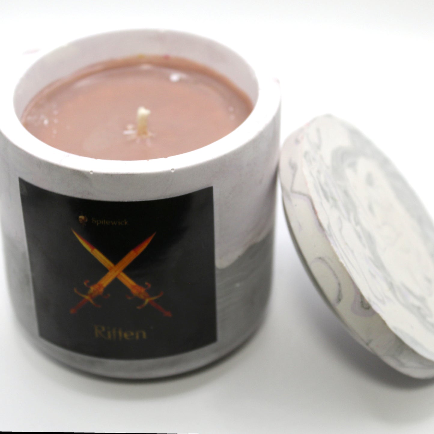 3/4 view of a soft purple and grey handcrafted candle holder featuring a black label adorned with an two crossed swords in stylized gold Celtic knotwork. Beneath the intricate design, the name riften is elegantly displayed in gold. The lid is removed and propped against the right side, revealing the tan candle inside. Set against a clean white background, this unique piece blends tradition with modern artistry, perfect for home decor, gifts, and personal expression.