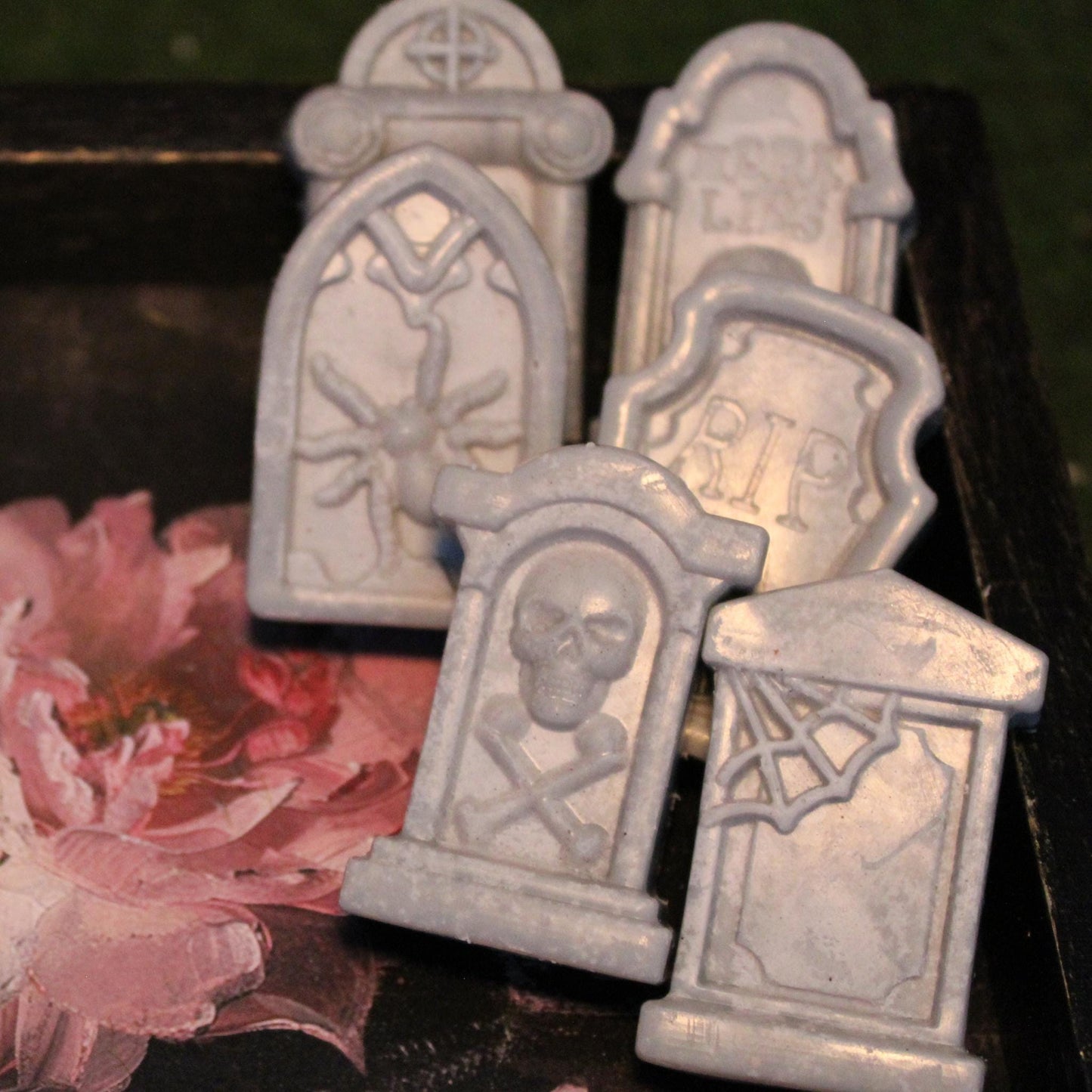 Five tombstone-shaped wax melts resting on an antique tray adorned with a cracked painted flower design and faded gold gilding. A haunting yet elegant gothic aesthetic, perfect for macabre decor, spooky ambiance, and alternative wax melt lovers.