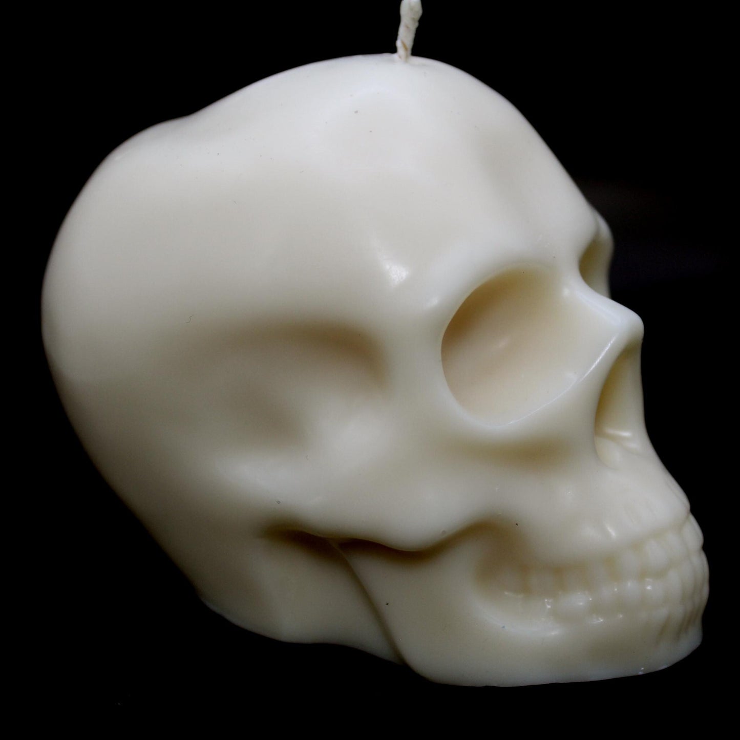 White skull-shaped wax candle against a black background, turned slightly to the right, showcasing detailed contours on the left side. A bold gothic decor piece perfect for dark aesthetic lovers, spooky home accents, and macabre candle enthusiasts.