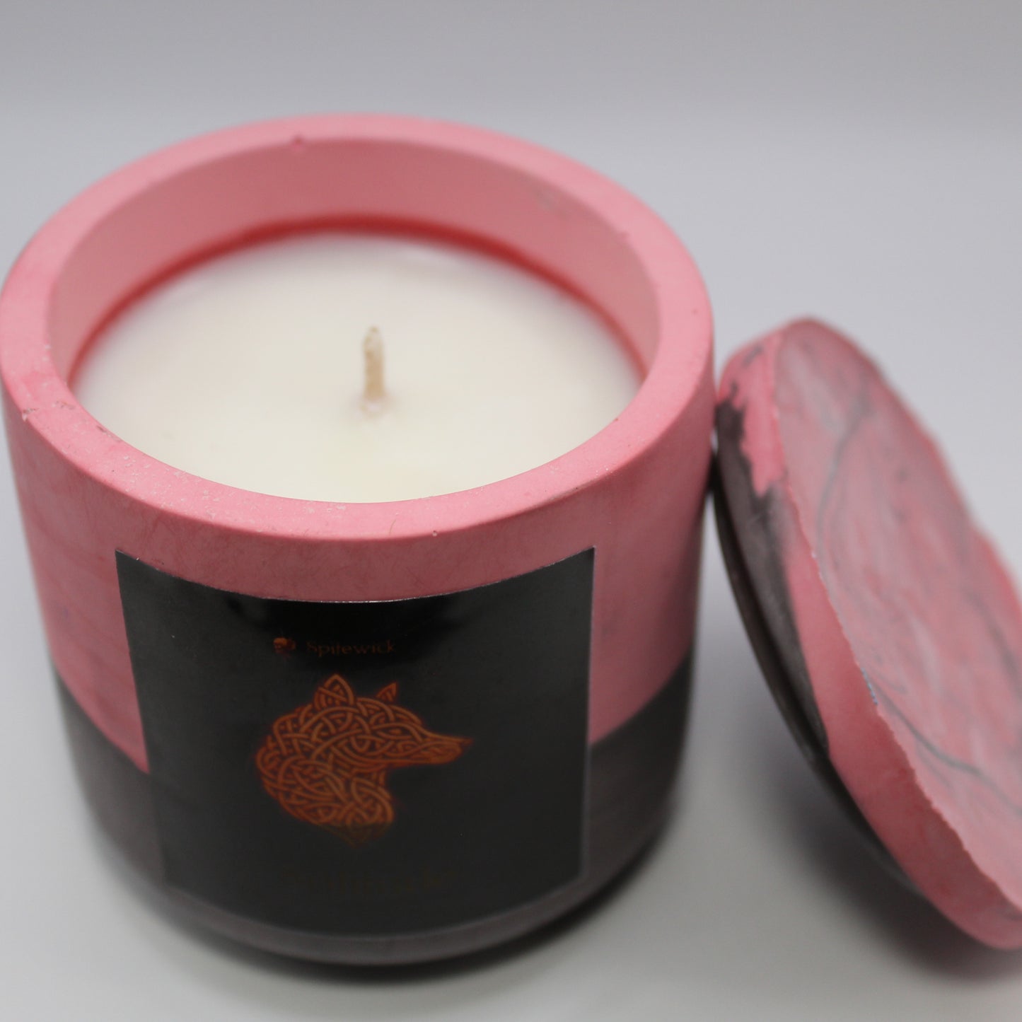 3/4 view of a red and black handcrafted candle holder featuring a black label adorned with a wolf in stylized gold Celtic knotwork. Beneath the intricate design, the name Solitude is elegantly displayed in gold. The lid is removed and propped against the right side, revealing the <color> candle inside. Set against a clean white background, this unique piece blends tradition with modern artistry, perfect for home decor, gifts, and personal expression.
