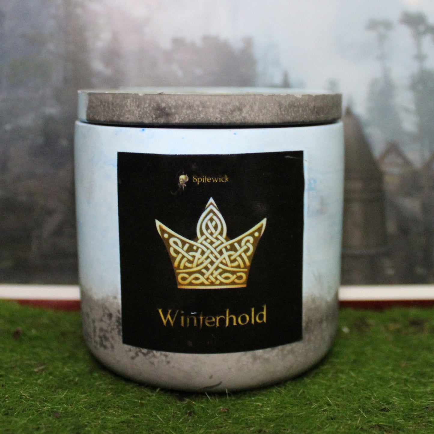 Front view of a handcrafted blue and black candle holder with a black label featuring a crown in gold Celtic knotwork. The name winterhold is elegantly printed in gold beneath the design. Set on grass, this piece blends artisan craftsmanship with bold identity, making it perfect for unique home decor, gifts, and statement lighting.