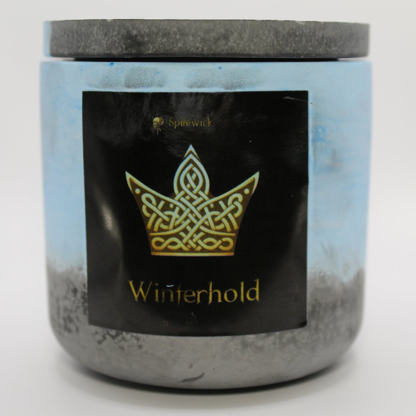 A blue and black candle with a sleek black label, featuring a Crown intricately designed in stylized gold Celtic knotwork. Beneath the design, the name Winterhold is elegantly printed in gold, adding a bold yet sophisticated touch. Set against a clean white background, this handcrafted candle blends tradition with modern artistry, perfect for unique home decor, gifts, and personal expression.