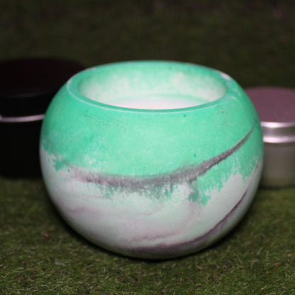 Handcrafted Ecocrete candle holder featuring the black, white, and green colors of the agender pride flag blended smoothly together. Product shot on grass with styling that includes a silver 2oz candle tin and black 4oz candle tin behind it, displaying the three available sizes of this LGBTQIA+ home decor piece.