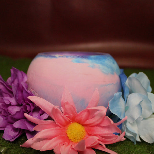 Handcrafted candle holder featuring the pink blue and purple hues of the bisexual pride flag, seamlessly blended together for a striking design. Set on grass with a burgundy vinyl backdrop, surrounded by an assortment of flowers mirroring the flag’s colors, creating a visually rich and identity-affirming scene. Perfect for LGBTQ+ home decor, pride gifts, and statement lighting.