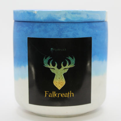 A blue and white candle holder with a sleek black label, featuring a deer intricately designed in stylized gold Celtic knotwork. Beneath the design, the name Falkreath is elegantly printed in gold, adding a bold yet sophisticated touch. Set against a clean white background, this handcrafted candle blends tradition with modern artistry, perfect for unique home decor, gifts, and personal expression.
