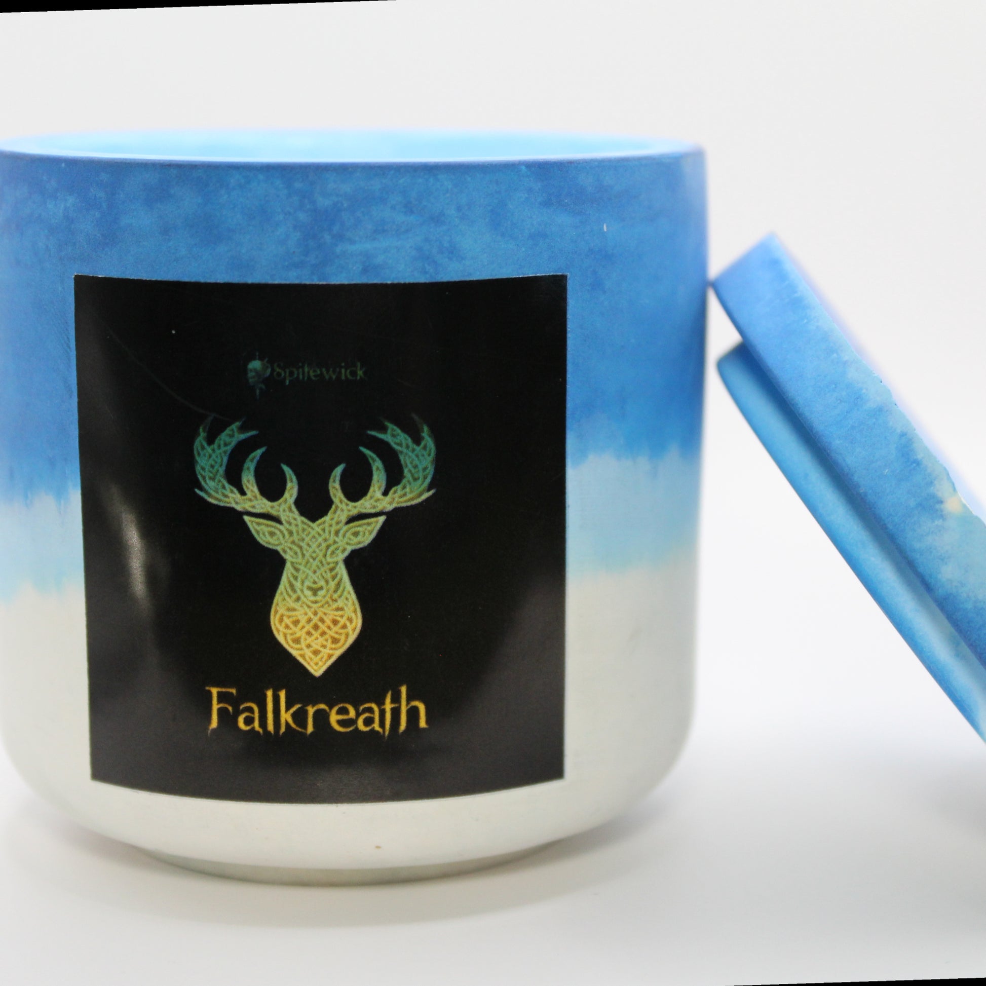 A blue and shite candle holder with a black label featuring a deer in elegant gold Celtic knotwork. The name Falkreath is displayed in gold beneath the intricate design, adding a bold, mystical touch. The lid is removed and propped against the right side, showcasing the full aesthetic. Set against a clean white background, this handcrafted candle merges tradition and modern artistry, perfect for unique home decor, gifts, and personal expression.