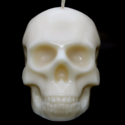 White skull-shaped wax candle set against a black background, staring directly into the camera with an eerie, haunting presence. A bold gothic decor piece perfect for dark aesthetic lovers, spooky home accents, and macabre candle enthusiasts."