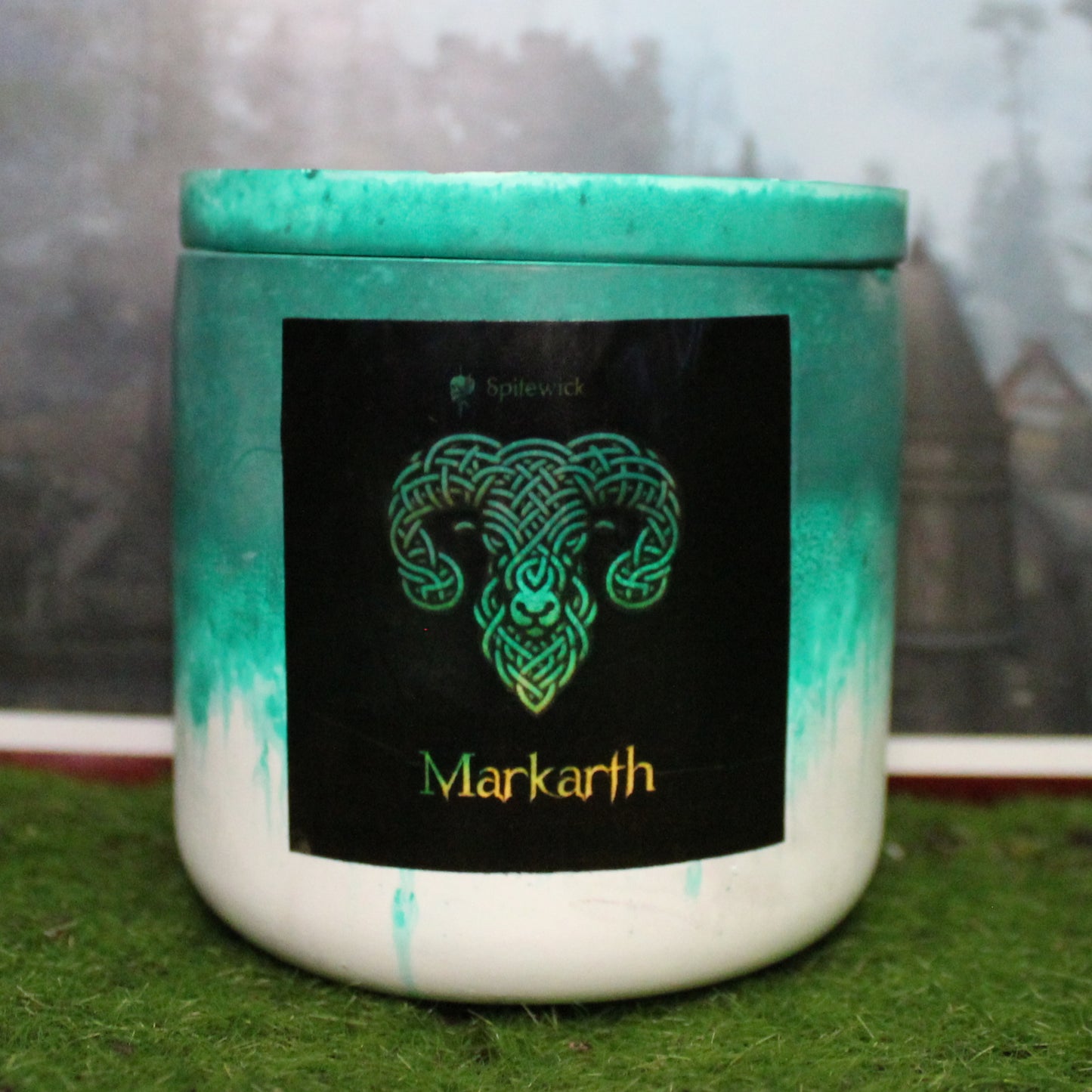 Front view of a handcrafted Green and white candle holder with a black label featuring a ram in gold Celtic knotwork. The name Markarth is elegantly printed in gold beneath the design. Set on grass, this piece blends artisan craftsmanship with bold identity, making it perfect for unique home decor, gifts, and statement lighting.