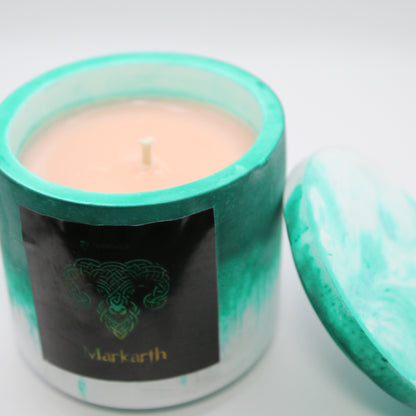 3/4 view of a green and white handcrafted candle holder featuring a black label adorned with a Ram in stylized gold Celtic knotwork. Beneath the intricate design, the name Markarth is elegantly displayed in gold. The lid is removed and propped against the right side, revealing the beige candle inside. Set against a clean white background, this unique piece blends tradition with modern artistry, perfect for home decor, gifts, and personal expression.