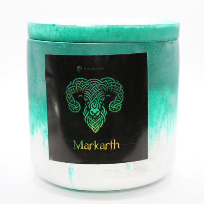 A green and white candle holder with a sleek black label, featuring a ram intricately designed in stylized gold Celtic knotwork. Beneath the design, the name Markarth is elegantly printed in gold, adding a bold yet sophisticated touch. Set against a clean white background, this handcrafted candle blends tradition with modern artistry, perfect for unique home decor, gifts, and personal expression.