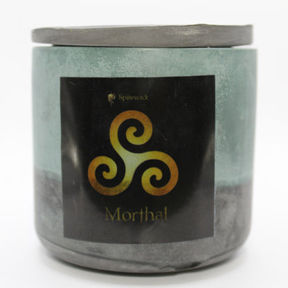 A green and black candle holder with a sleek black label, featuring a Triskele intricately designed in stylized gold. Beneath the design, the name Morthal is elegantly printed in gold, adding a bold yet sophisticated touch. Set against a clean white background, this handcrafted candle blends tradition with modern artistry, perfect for unique home decor, gifts, and personal expression.
