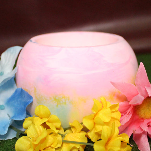 Handcrafted candle holder featuring the pink, yellow, and blue hues of the pansexual pride flag, seamlessly blended together for a striking design. Set on grass with a burgundy vinyl backdrop, surrounded by an assortment of flowers mirroring the flag’s colors, creating a visually rich and identity-affirming scene. Perfect for LGBTQ+ home decor, pride gifts, and statement lighting.