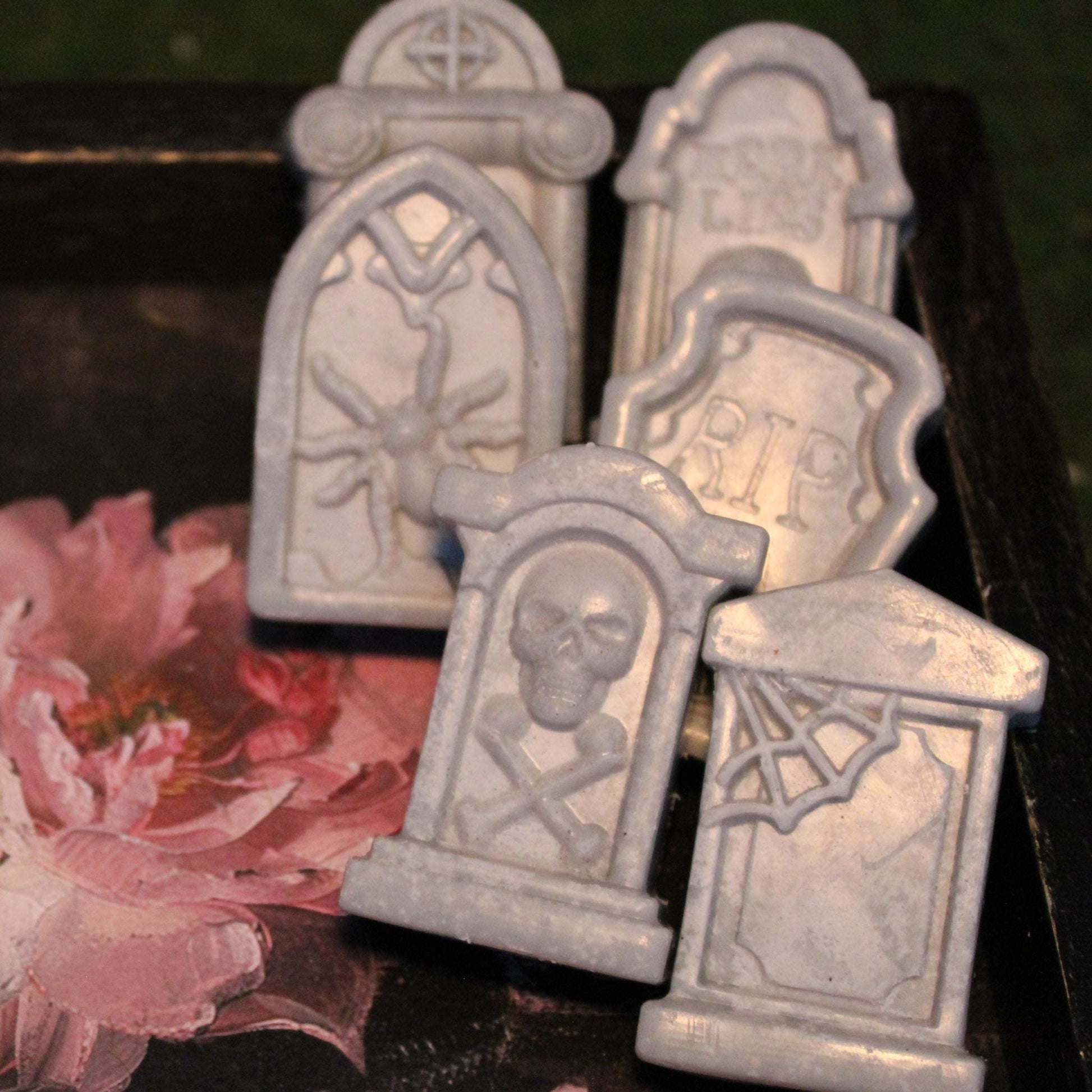 Five tombstone-shaped wax melts resting on an antique tray adorned with a cracked painted flower design and faded gold gilding. A haunting yet elegant gothic aesthetic, perfect for macabre decor, spooky ambiance, and alternative wax melt lovers.