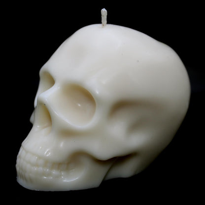 White skull-shaped wax candle against a black background, turned slightly to the left, highlighting intricate details on the right side. A bold gothic decor piece perfect for dark aesthetic lovers, spooky home accents, and macabre candle enthusiasts.