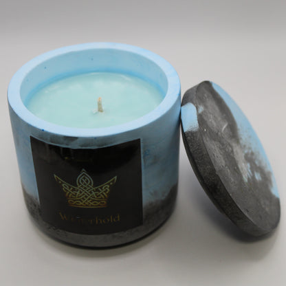 3/4 view of a blue and black handcrafted candle holder featuring a black label adorned with a Crown in stylized gold Celtic knotwork. Beneath the intricate design, the name Winterhold is elegantly displayed in gold. The lid is removed and propped against the right side, revealing the blue candle inside. Set against a clean white background, this unique piece blends tradition with modern artistry, perfect for home decor, gifts, and personal expression.